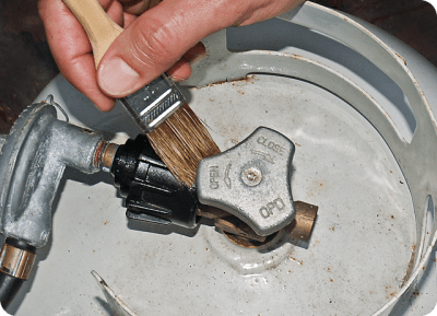 Hand applying leak detector solution to propane cylinder valve